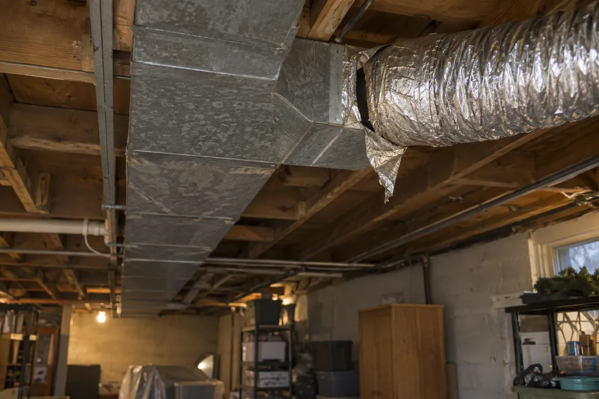 Insulated flexible duct pulling away from a sheet-metal trunk line in a basement ceiling